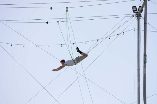 A trapeze artist swings and reaches for the bar in the air