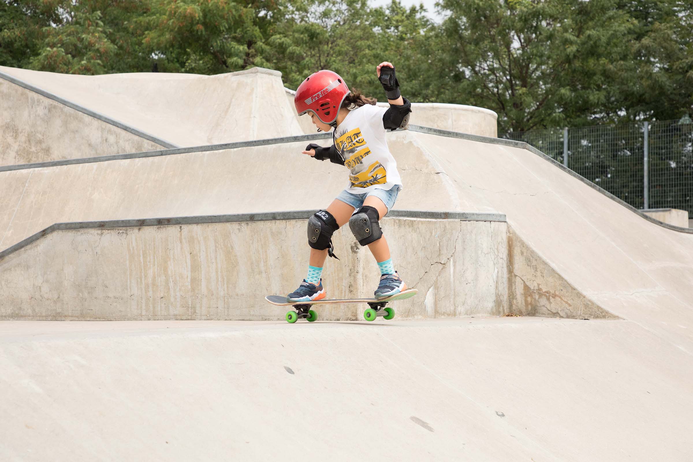 A kid skateboarder in a red helmet coasting around the skatepark