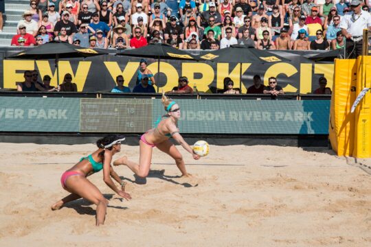 A volleyball player and her teammate crouch to hit the ball