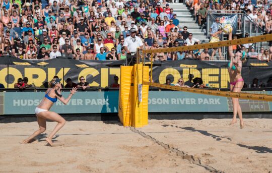 The volleyball flies over the net on the sandy court