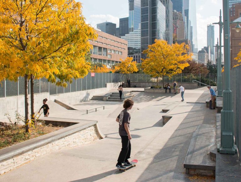 Orange and yellow trees align the Tribeca Skatepark where active kids enjoy spinning around