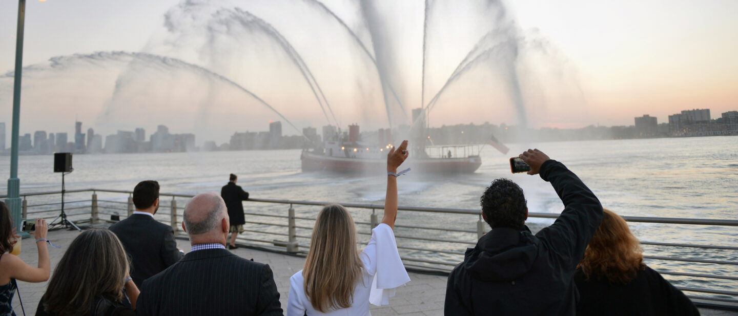 A fireboat on the Hudson River blasts streams of water into the air as spectators watch