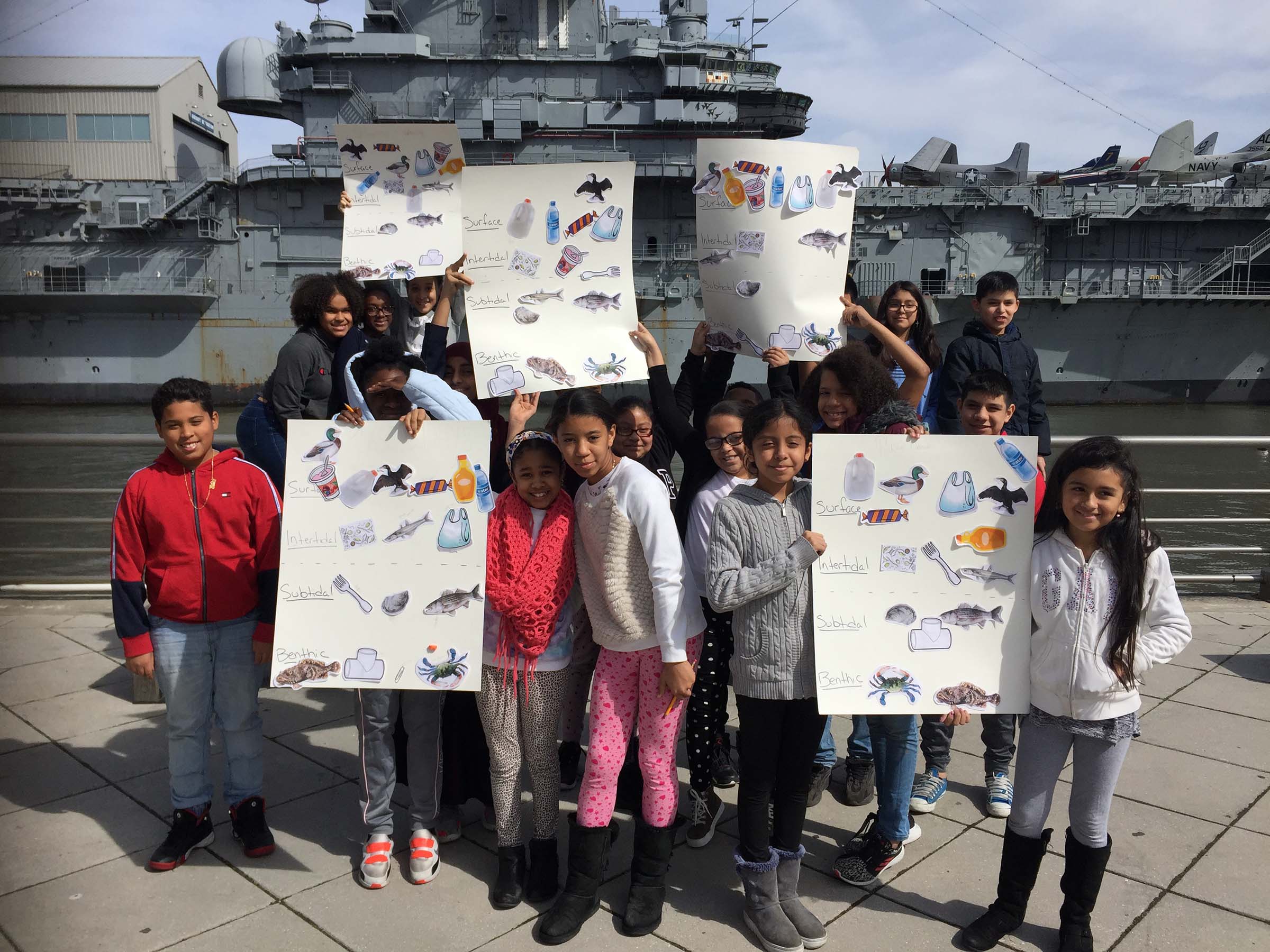Kids pos with fish posters in front of the Intrepid vessel