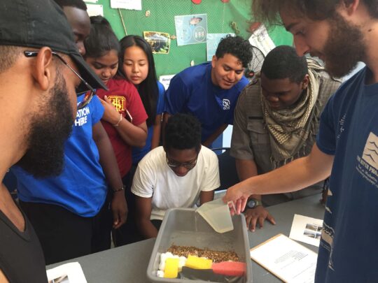 A Park educator pours water into the dirt to demonstrate a lesson