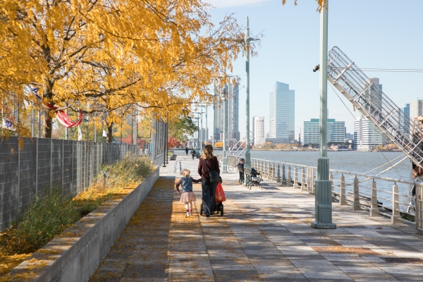 A parent and child walk down Pier 25 as orange leaves fall off the trees