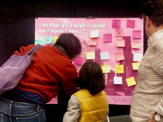 Community members post post it notes on a board about their ideas for Pier 97