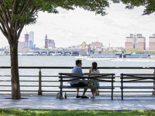 Two park visitors sit on a bench looking out to the hudson river