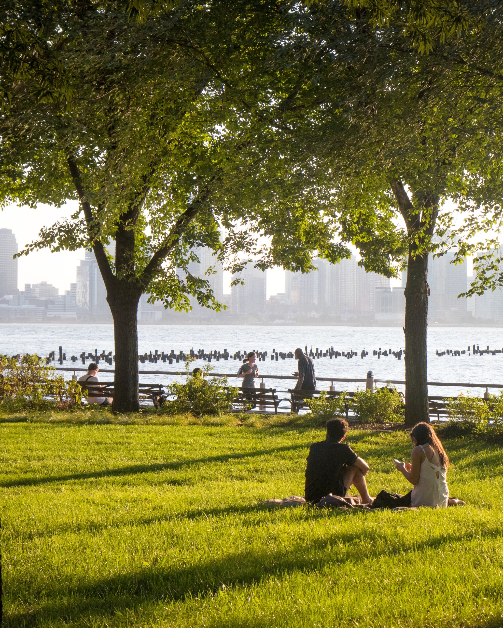Two Park patrons enjoy a greenwich village picnic on the green Pier 46 lawns with a view of the Hudson River at HRPK