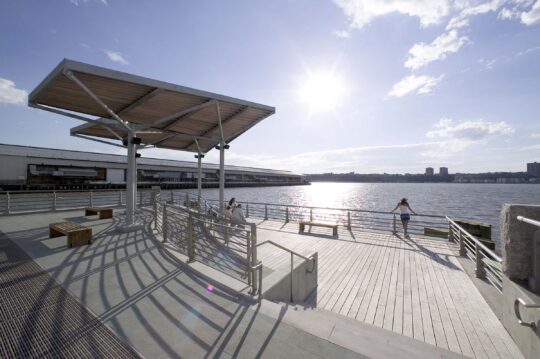 Park patrons watch the sun's rays on the water along Pier 95 at Hudson RIver Park