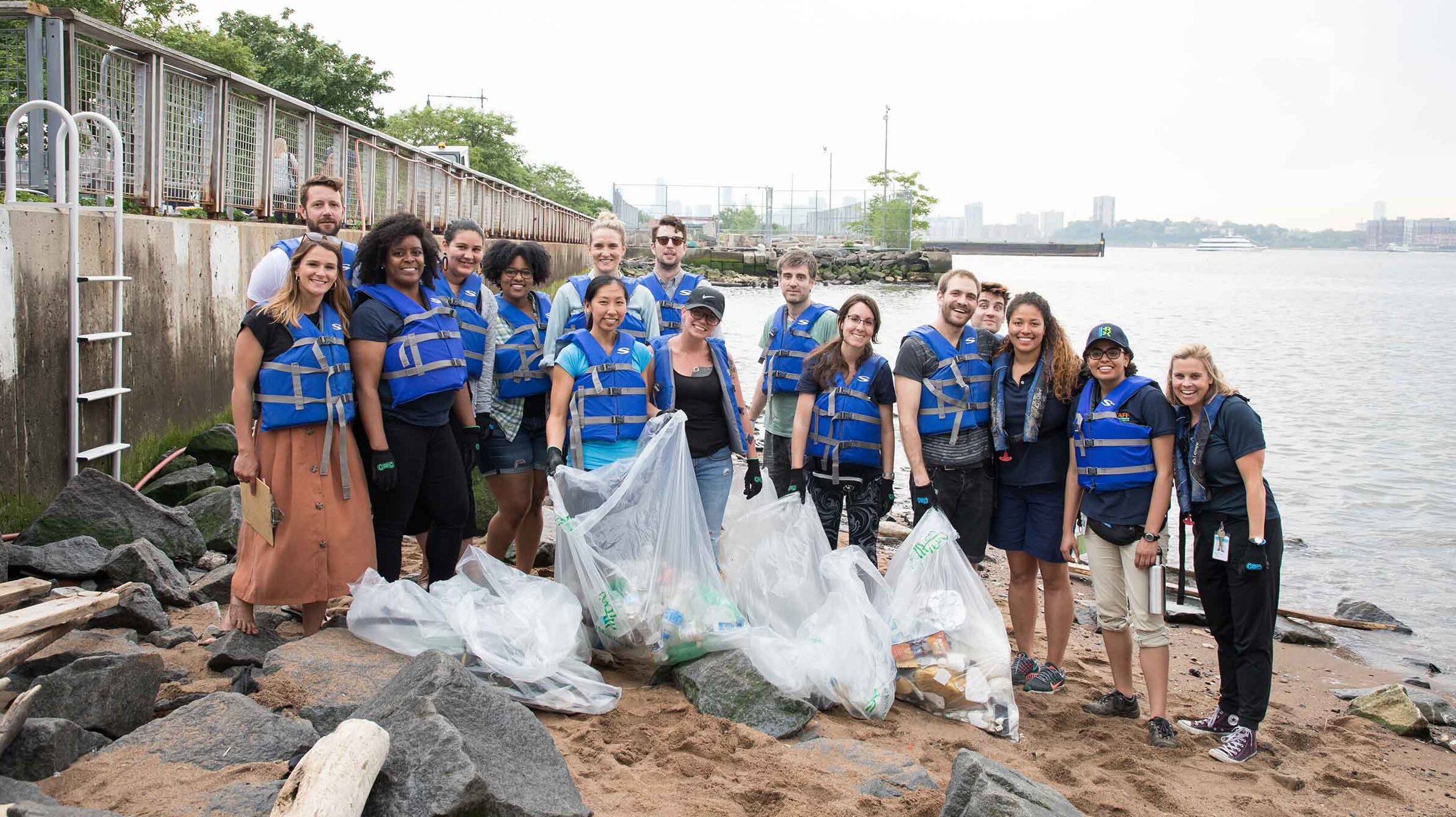 A group of volunteers cleaning up plastic at the shoreline and posing for the camera