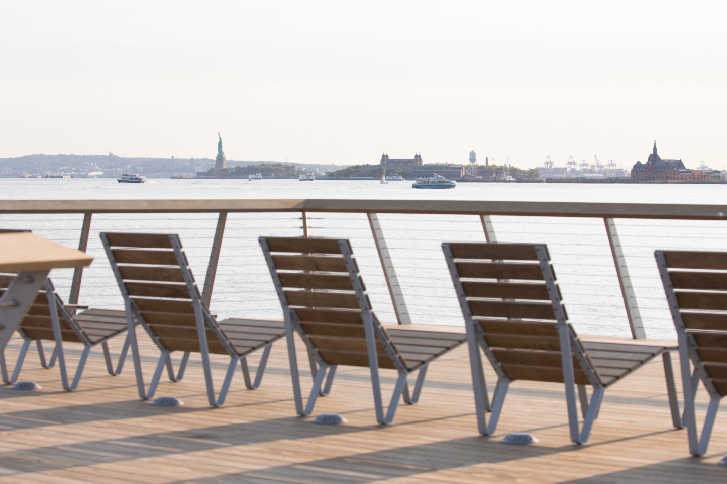 A row of chairs looking over the Hudson River face a sunny view of the Statue of Liberty from Hudson River Park's Pier 26