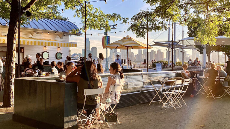 People sitting at tables at Drift In restaurant in Hudson River Park at sunset