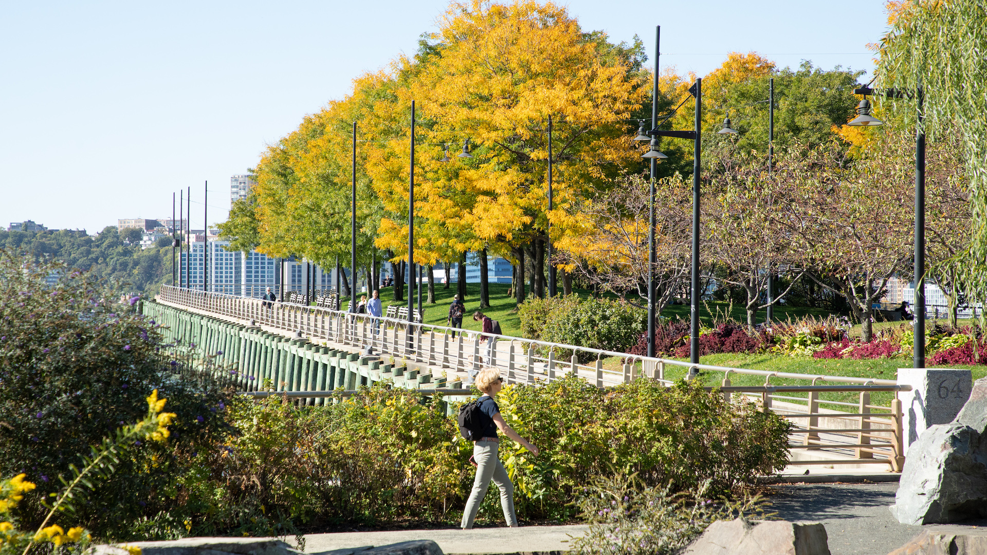 Person walks through stone field in Chelsea in Hudson River Park, fall leaves on Pier 64 in the background