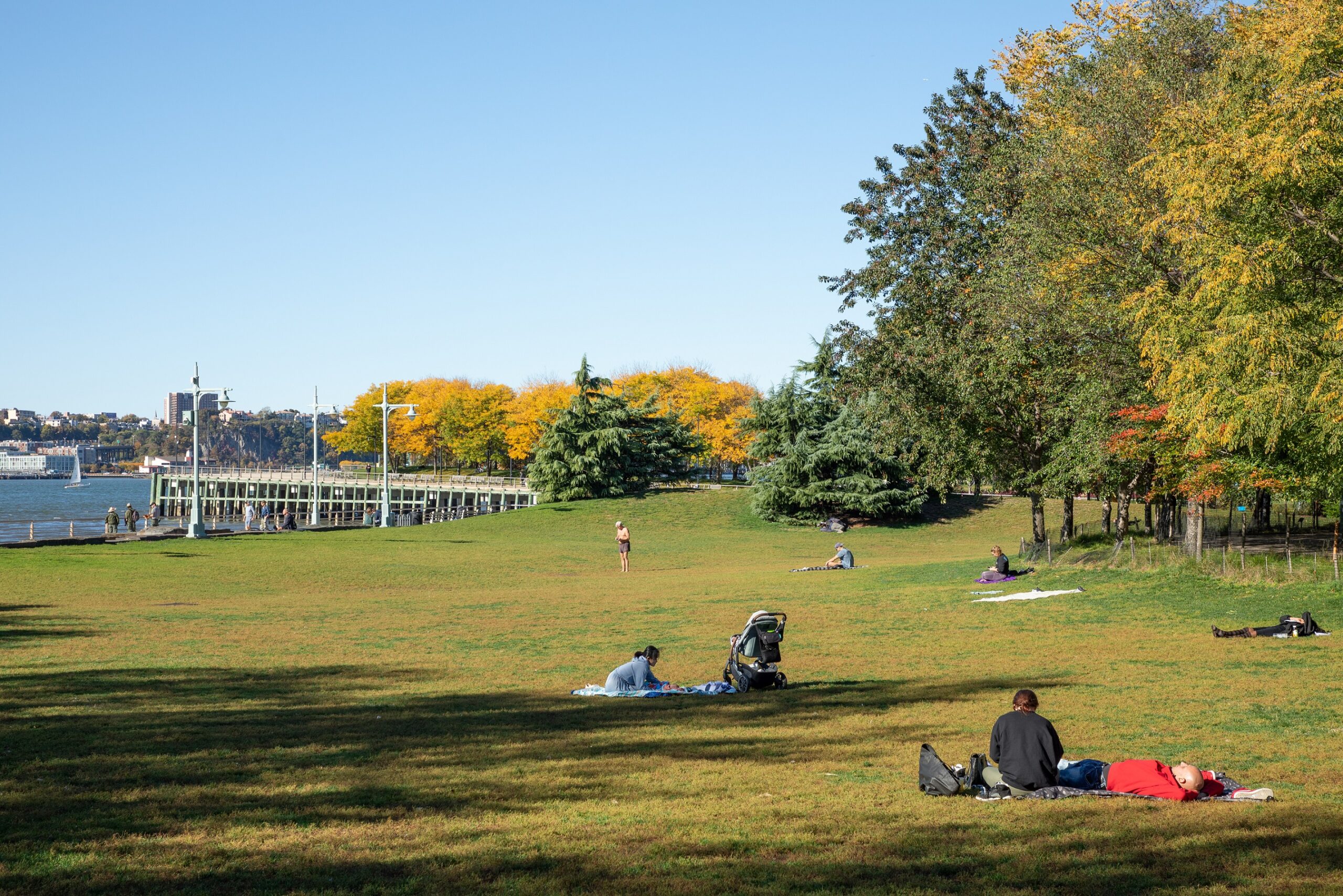 People picnic on sunny fall day on Hudson River Park's Pier 63, fall foliage in the background