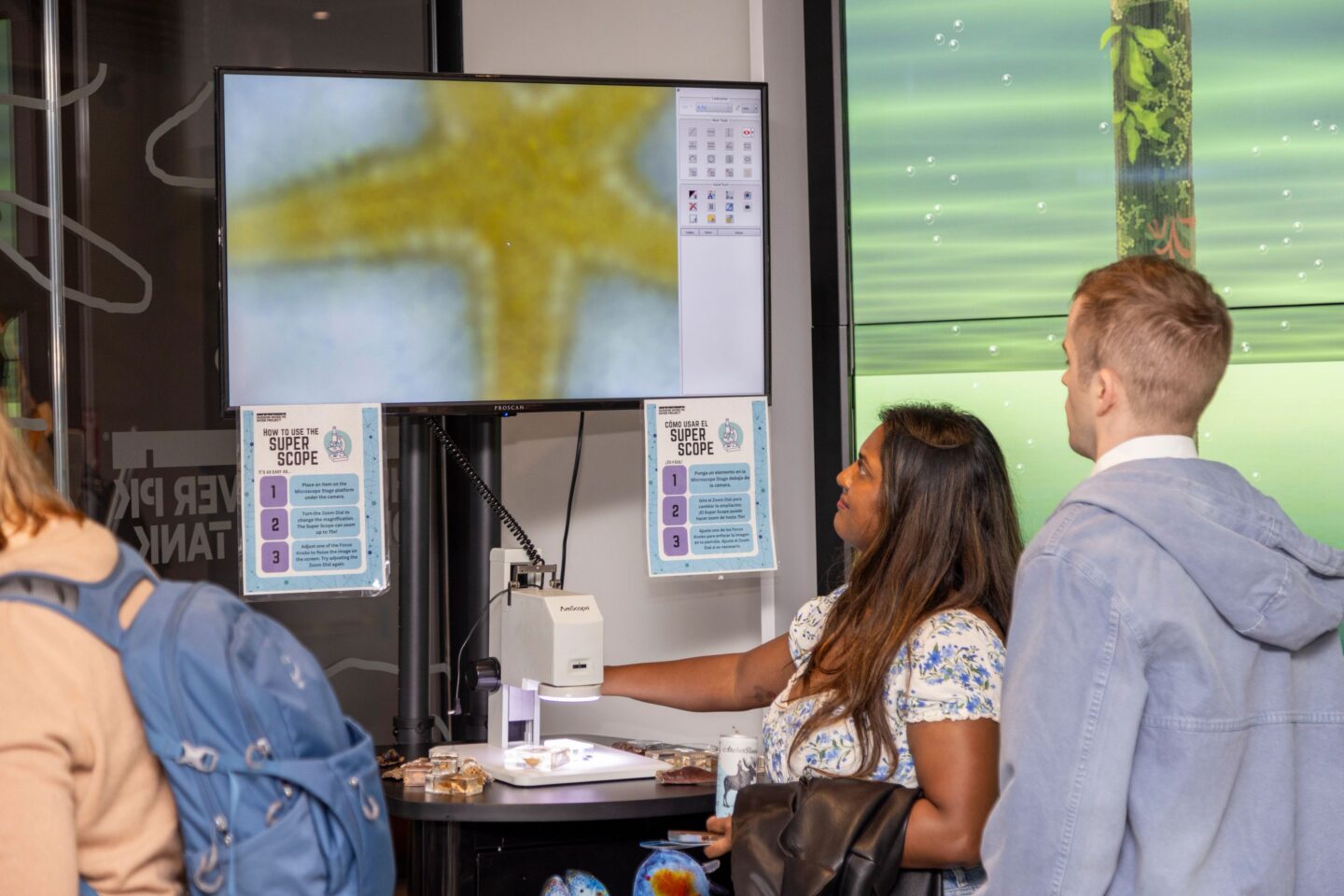 Two people look at a microscope slide via a display screen at the Pier 57 Discovery Tank