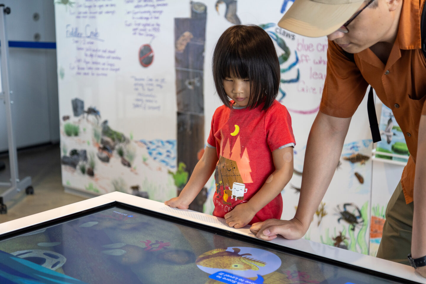 A student interacts with a touchscreen display at the Pier 57 Discovery Tank while a parent watches on