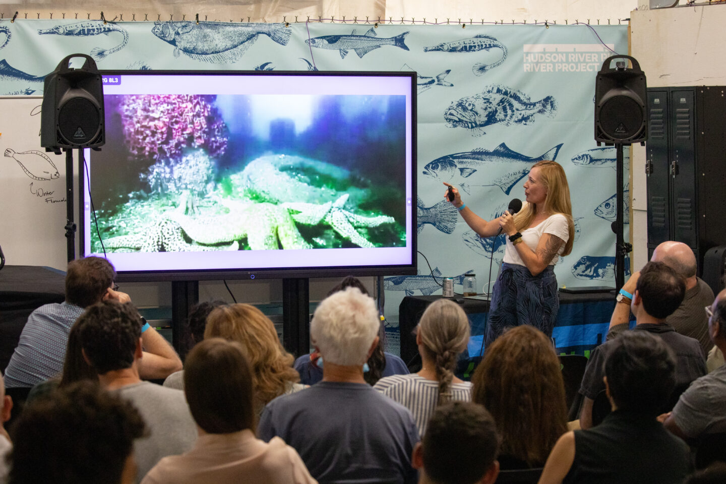 A scientist giving a presentation to an audience using a digital screen, as part of Hudson River Park's Ask a Scientist event series