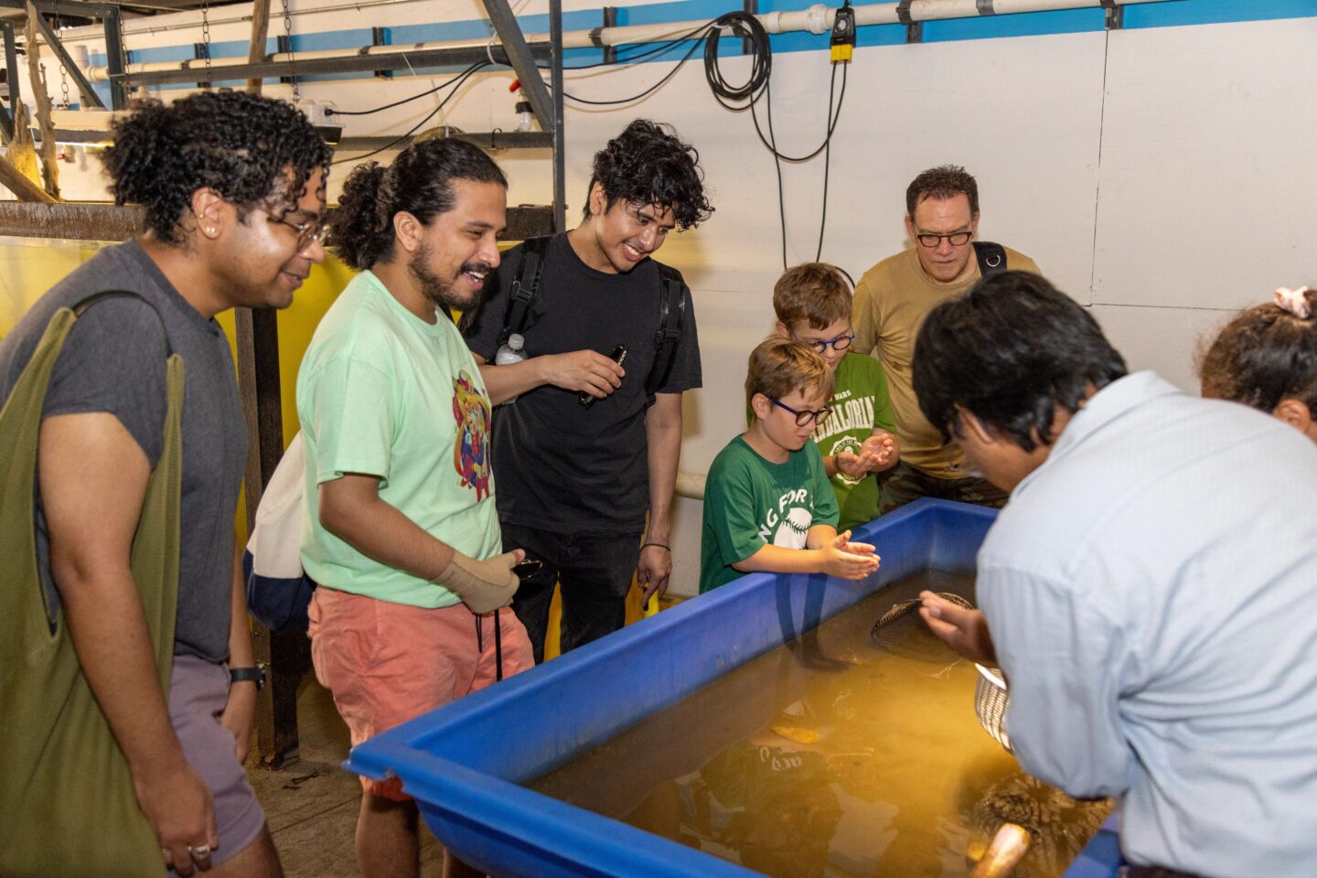 A group of visitors to Hudson River Park's Pier 40 Wetlab gather around a touch tank station