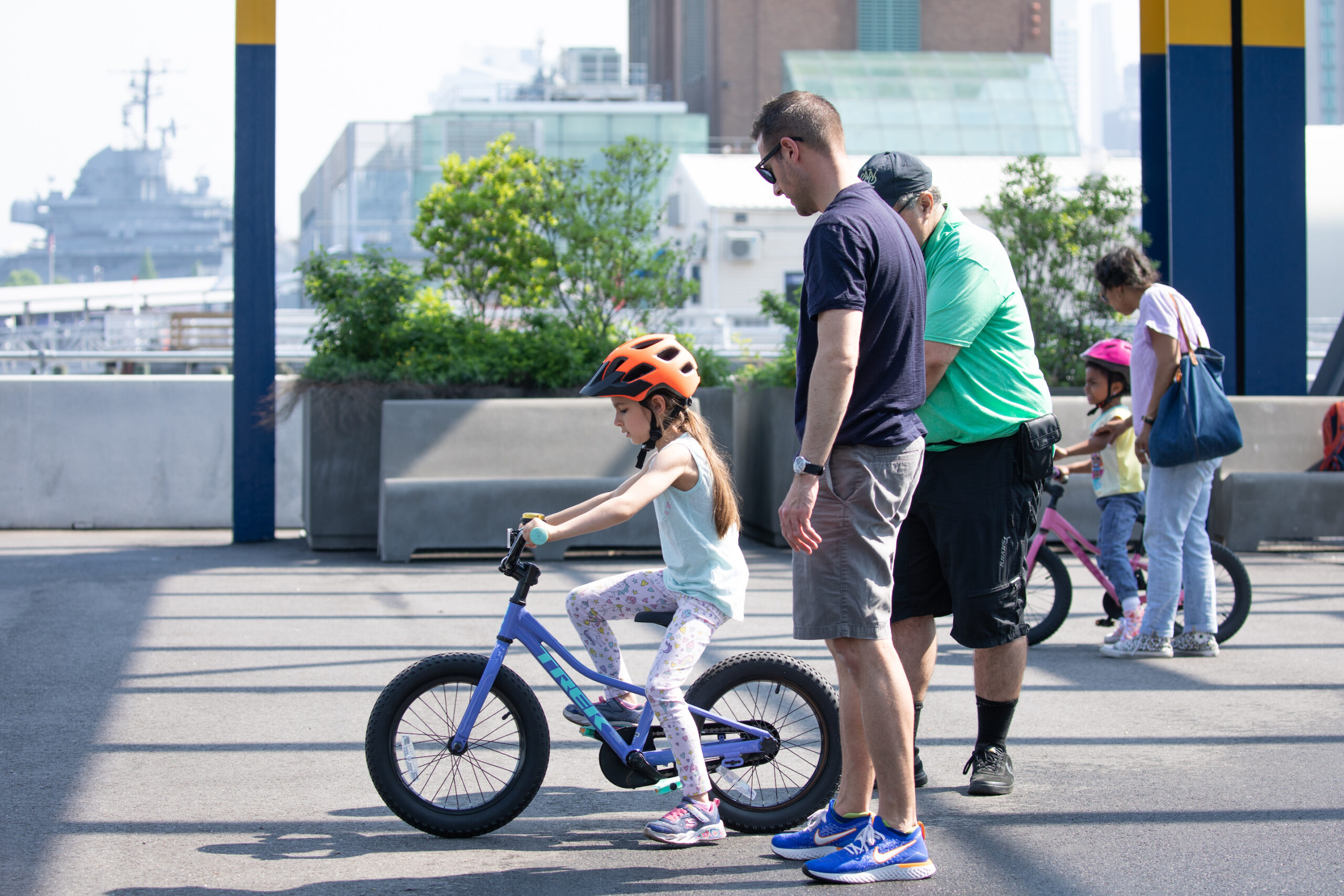 A Bike New York Bike Skills instructor teaching a girl how to ride a bike while her parent looks on