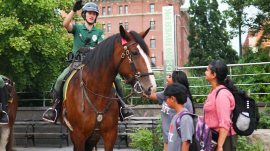 A Parks Enforcement Patrol officer on horseback speaks to three Park visitors