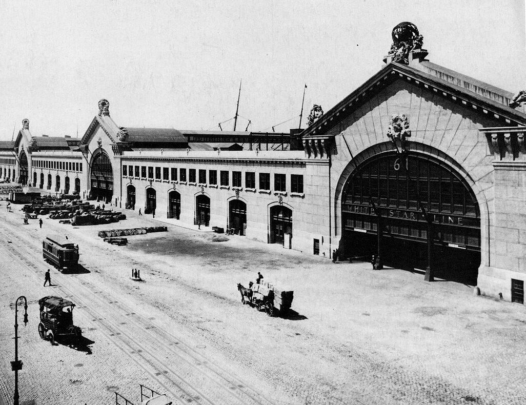 Historic black-and-white photo of Chelsea Piers with arched pier entrances, a streetcar, horse-drawn wagons and early automobiles.