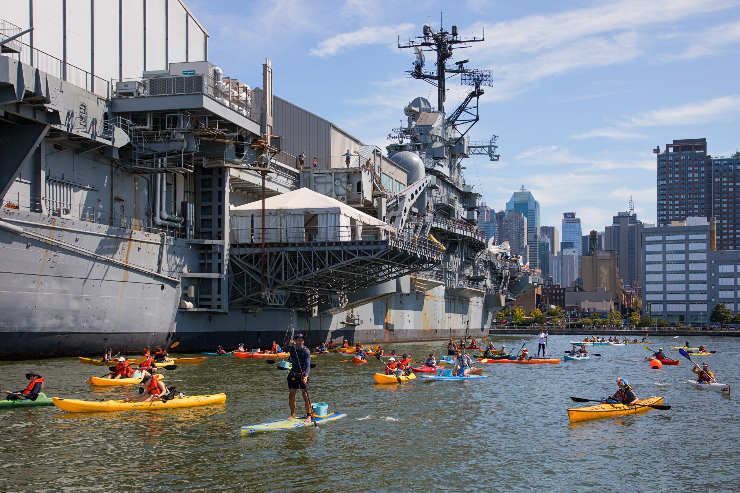 Kayakers paddling alongside the USS Intrepid.