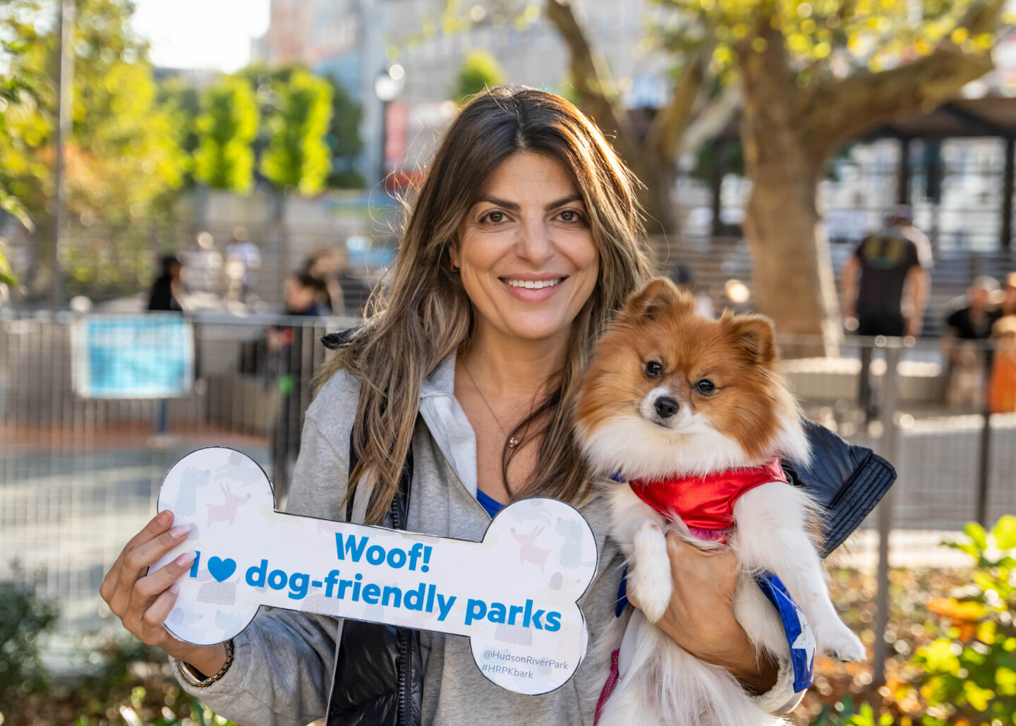 woman holding small dog and sign about dog-friendly parks smiles for camera