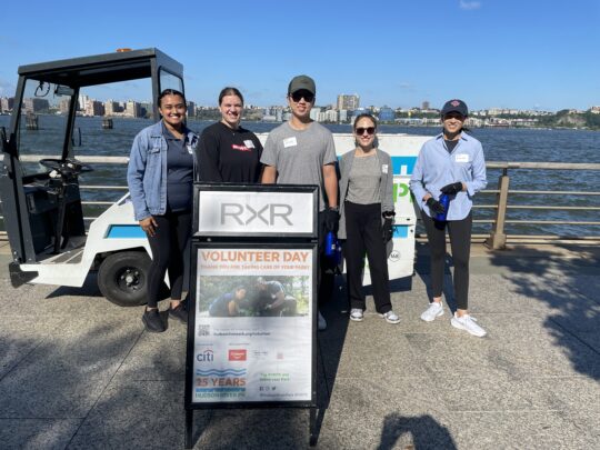 Five volunteers from RXR smile in front of a Hudson River Park Motrec vehicle