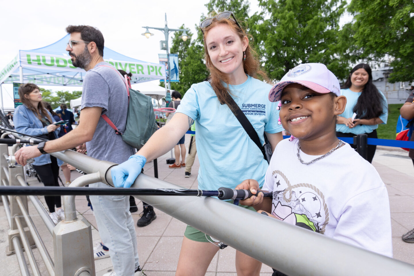 An HRPK River Project staffer stands with a student as they cast a fishing rod off of Pier 84