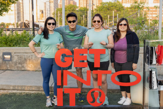 Four people gathered behind a sign with a lululemon logo and the words "Get Into It"