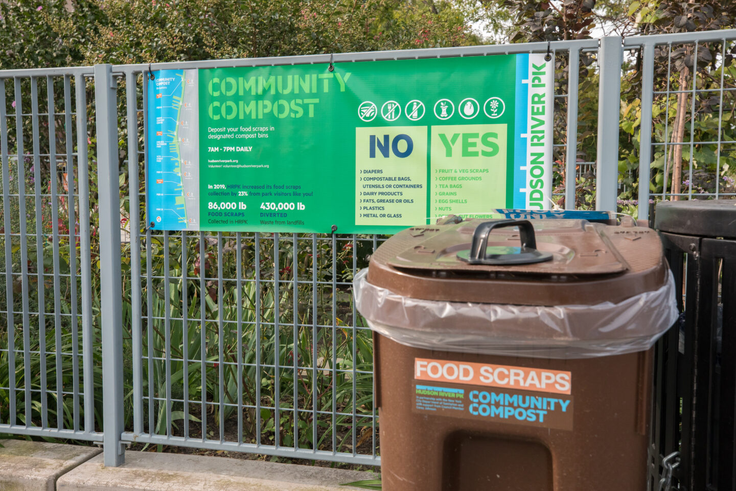 A compost drop-off container in front of a sign that provides instructions for composting