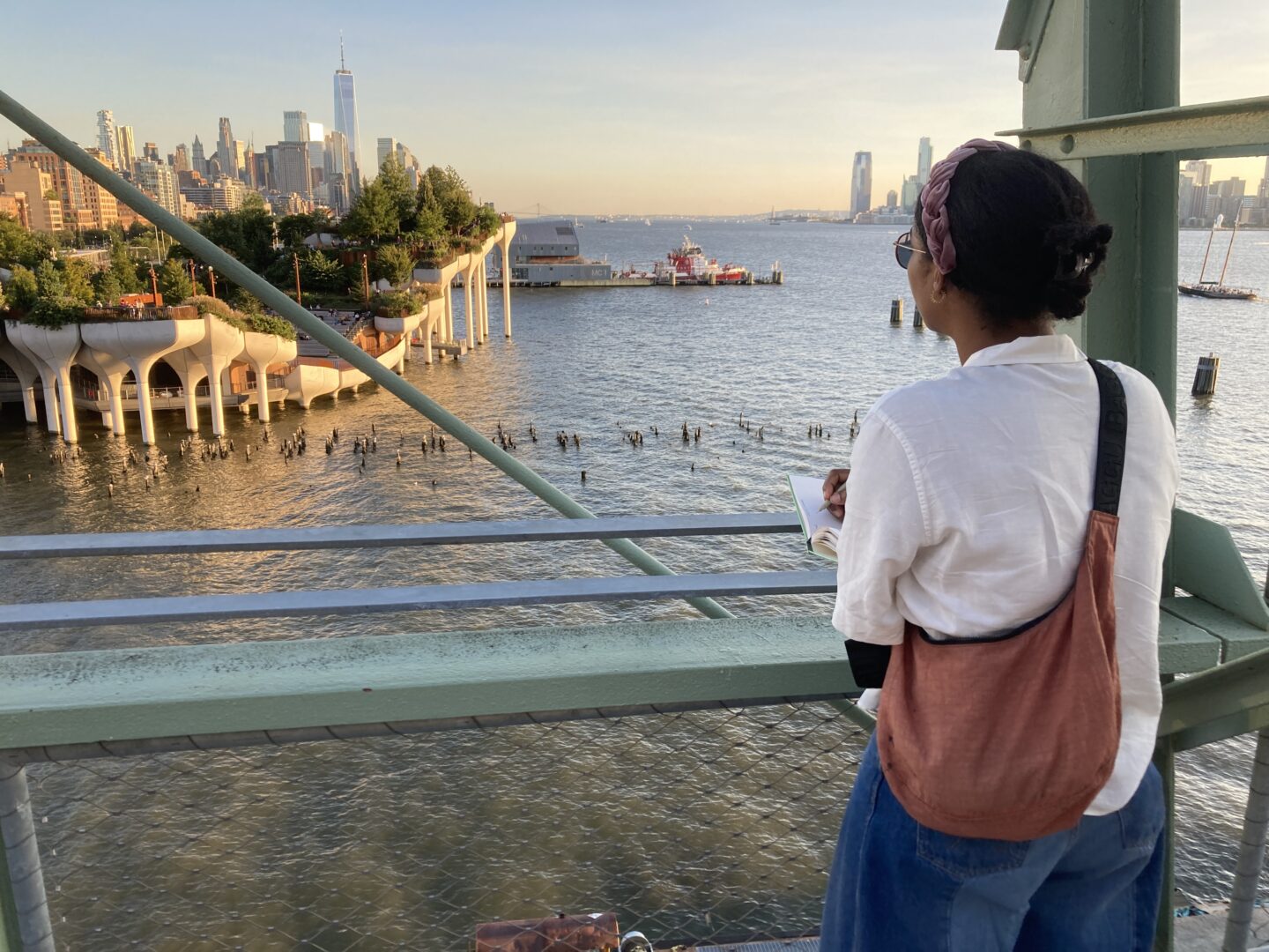 A person writing in a Nature Poetry class from the Pier 57 Rooftop Park, looking out toward Little Island and Lower Manhattan
