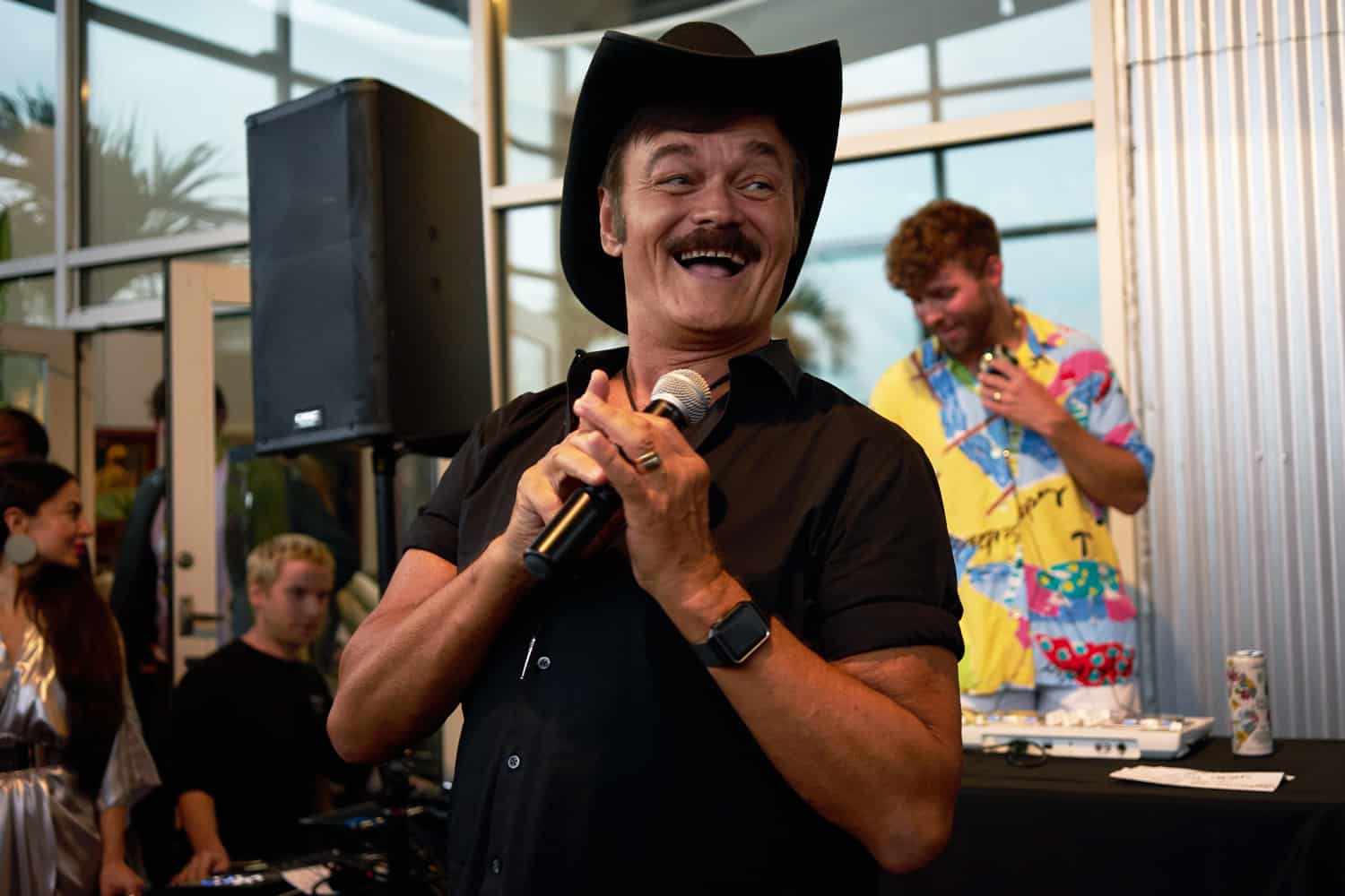 Randy Jones singing into a microphone in front of a DJ