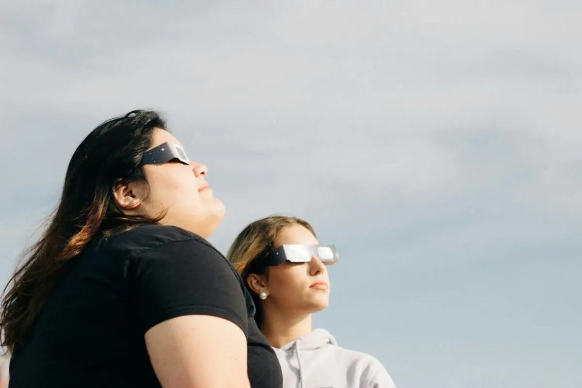 Two people looking up at the sky while wearing eclipse safety glasses