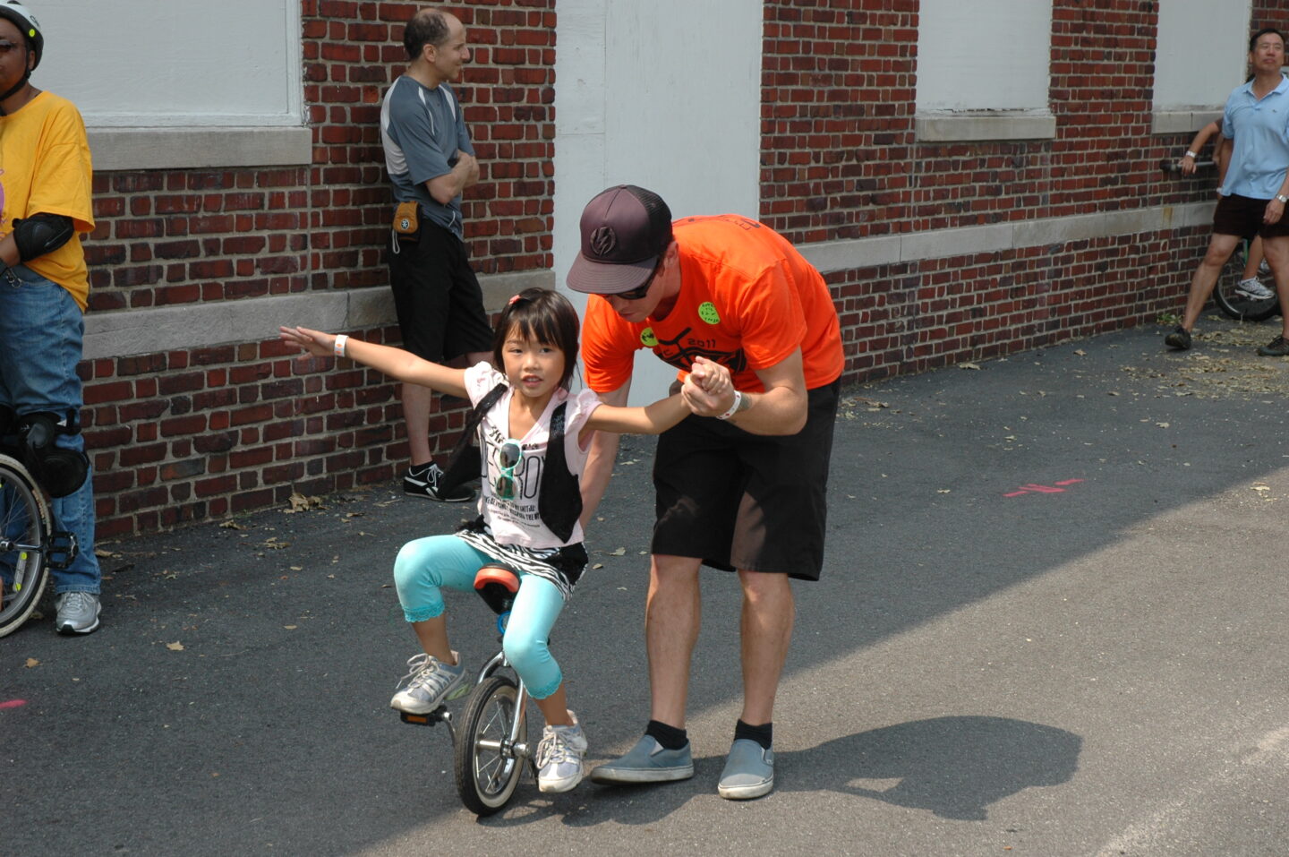 A parent guides a child riding a unicycle, holding their hand for balance