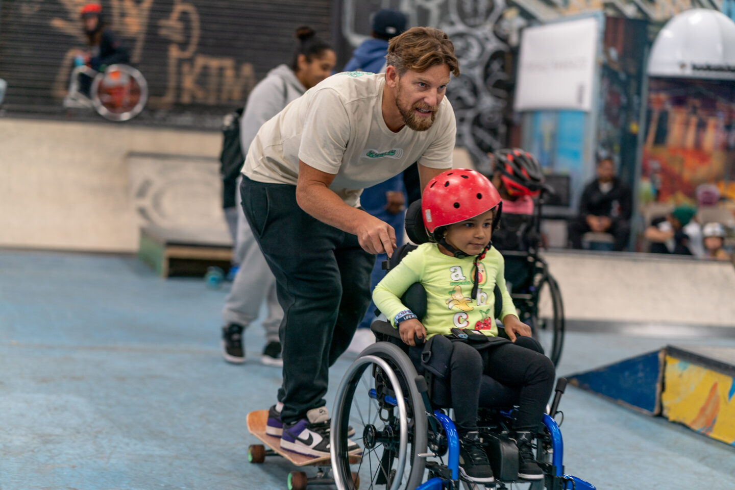 A person on a skateboard pushes a child in a wheelchair at a skatepark