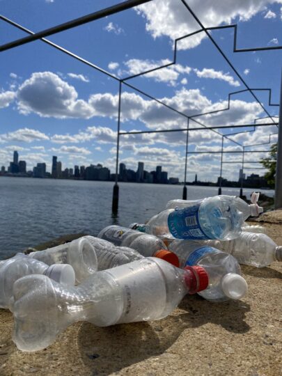 Plastic bottles collected near Gansevoort Peninsula sit on the shoreline. David Hammons' "Day's End" structure is visible in the background.