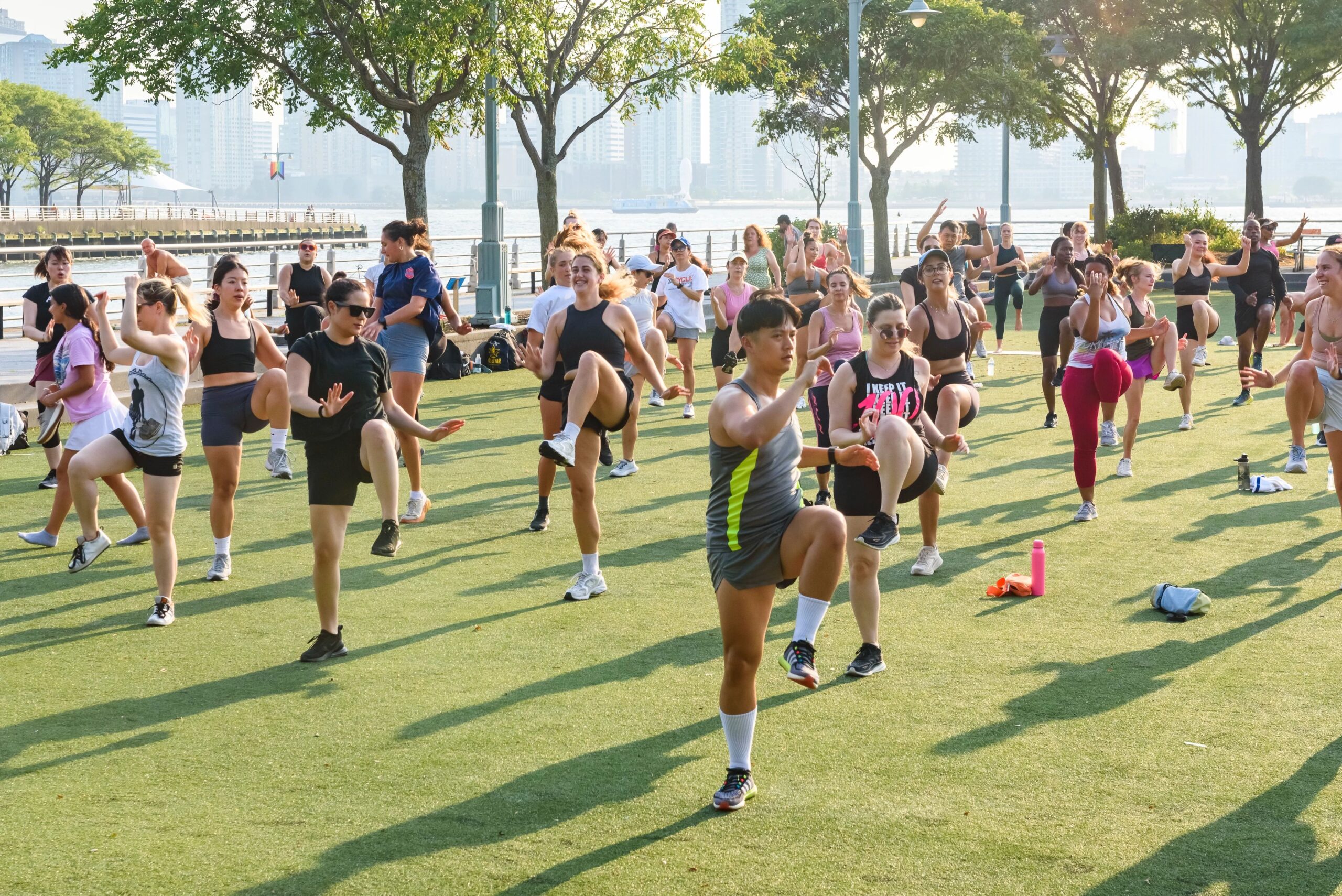 Participants in a Healthy on the Hudson fitness class kick up in unison on the Pier 46 turf field