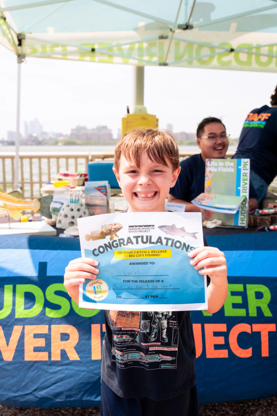 A child smiling and holding a certificate for catching a fish at HRPK's Big City Fishing program