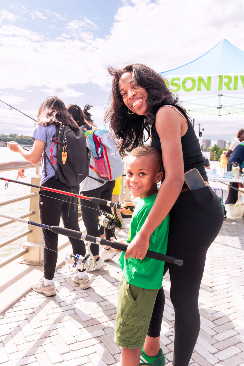 A parent and a child holding a fishing pole at a Big City Fishing event on Pier 97