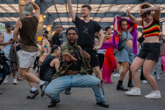 A dancer squatting and holding a pose among a group of dancers at Pier 76