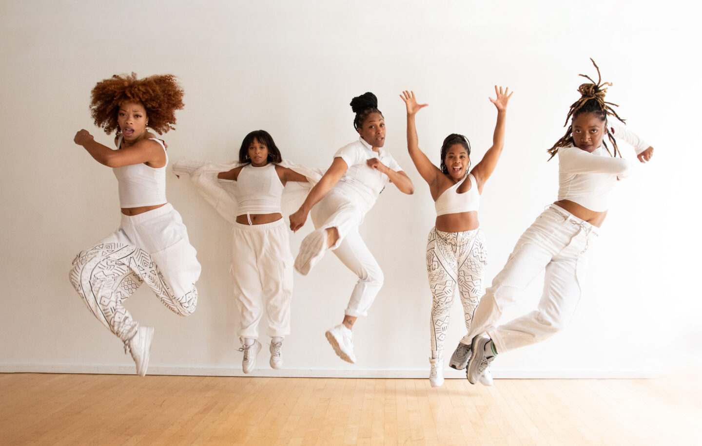 Five members of Ladies of Hip Hop jumping and holding a pose in mid-air in a dance studio
