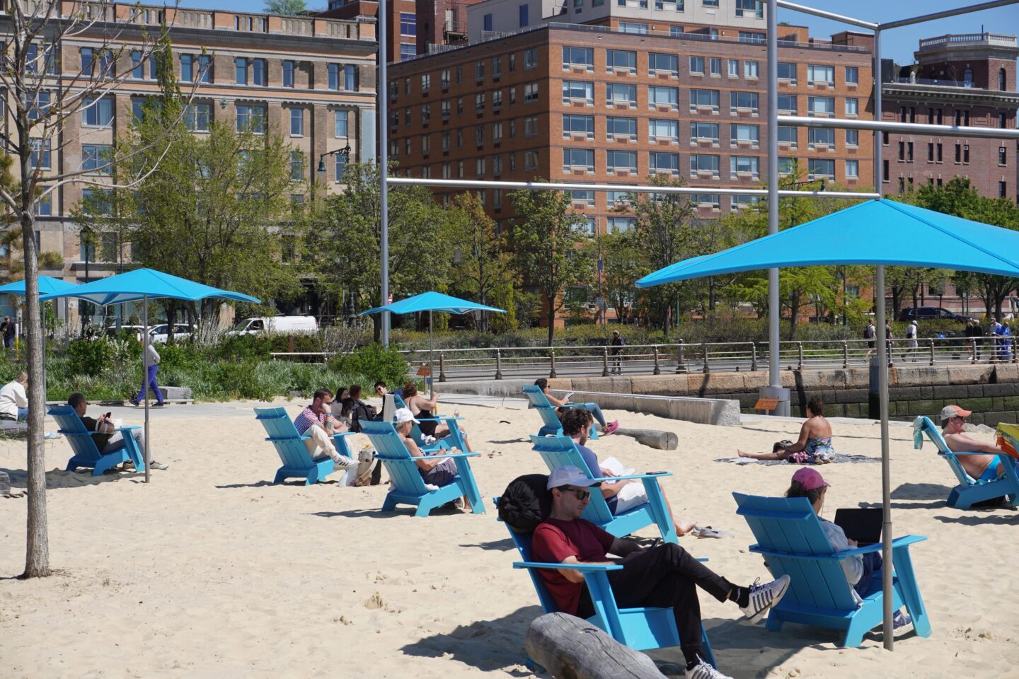 People sitting in the sand in chairs and under umbrellas on the Gansevoort Peninsula Sand Bluff