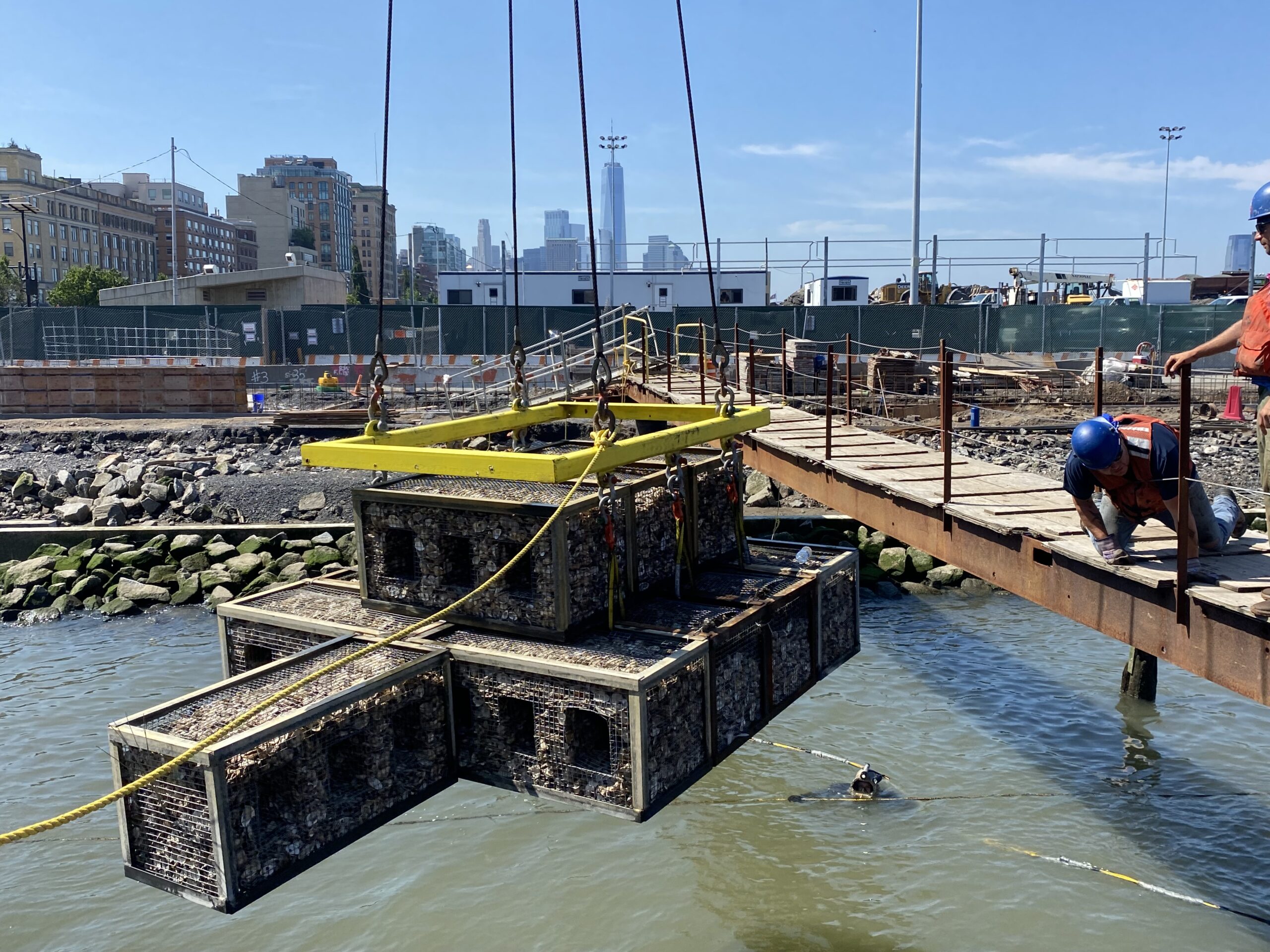 A gabion hoisted by a crane is lowered into the Hudson River on the north side of Gansevoort Peninsula