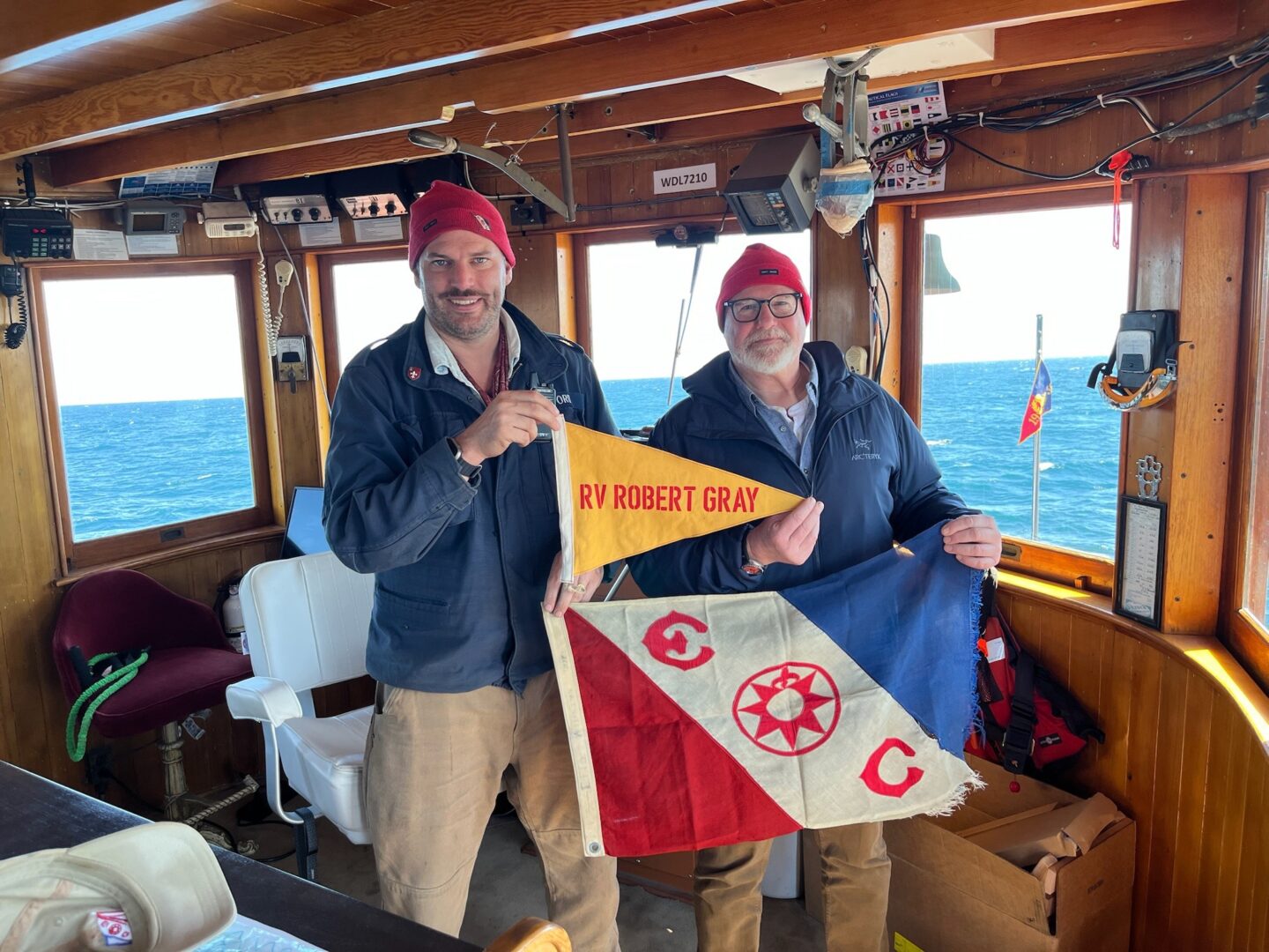 Two staff members on the Research Vessel Robert Gray hold a pennant and a flag