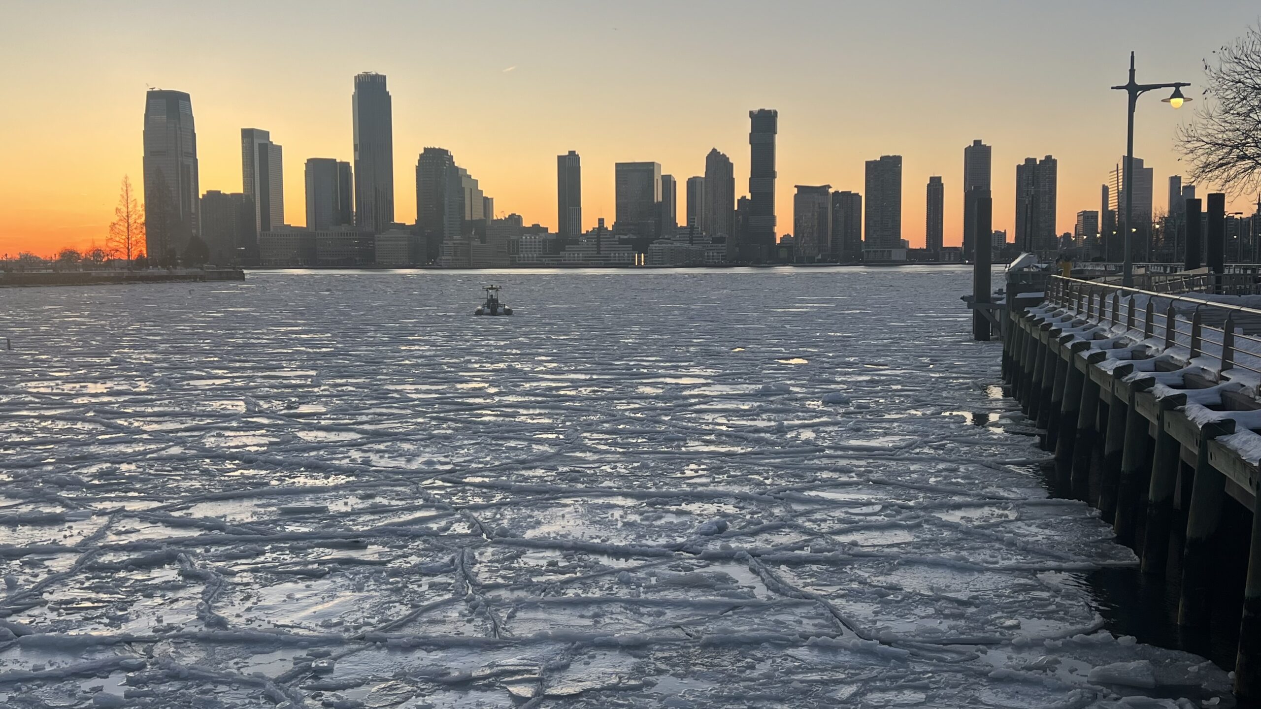 Sunset over ice floes on the Hudson River, a pier railing on the north side of the photo