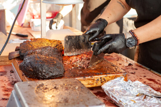 A closeup of a food vendor chopping smoked meat