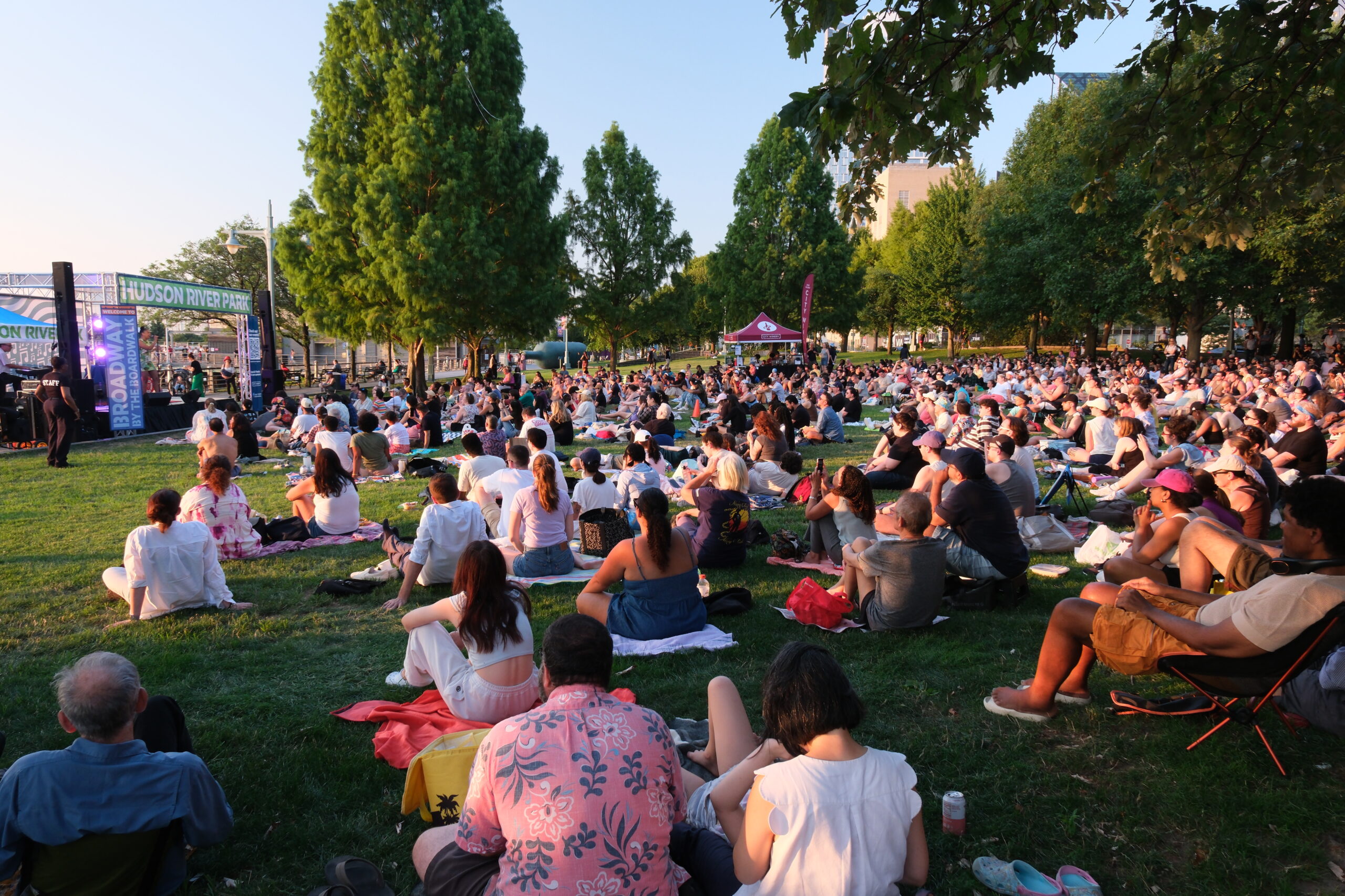 A large crowd seated on the Clinton Cove lawn enjoys a Broadway by the Boardwalk performance