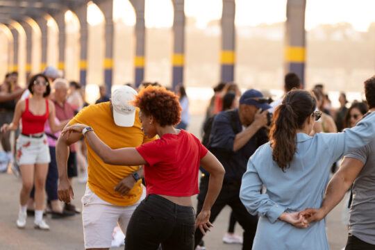 People dancing under a covered Hudson River Park pier during an outdoor summer event.