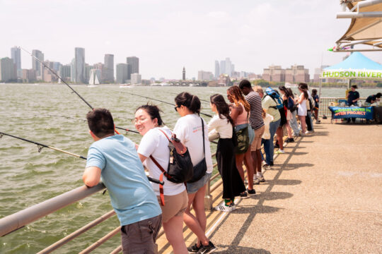 People holding fishing rods over the railing at Pier 51 during a Big City Fishing event